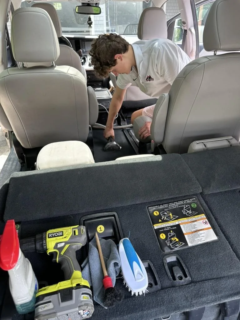 Hanover Detailing team member vacuuming between the seats of a minivan